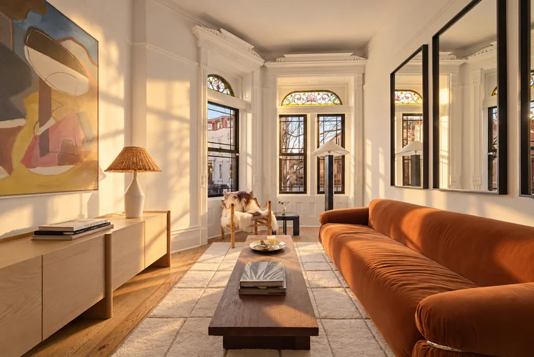 Golden-hour living room with an orange sofa, wood credenza and stained-glass bay windows at 731 Putnam