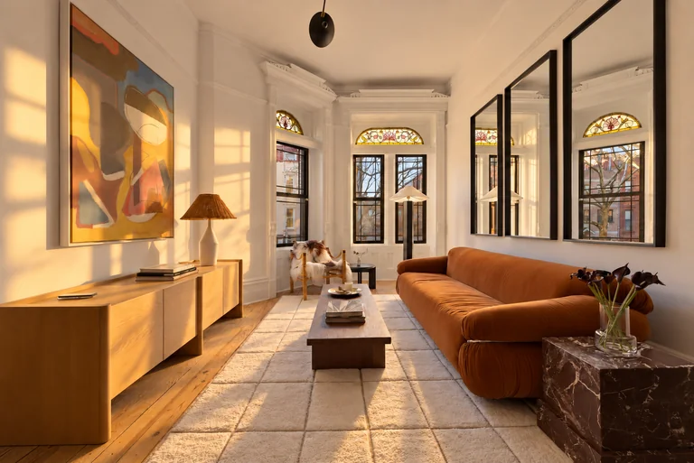 Wide living-room view with an orange sofa, three wall mirrors and stained-glass windows at 731 Putnam