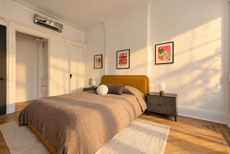 Bedroom with a mustard headboard, three framed prints and wood flooring in warm afternoon light.