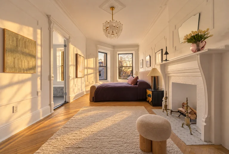 Bedroom with a white fireplace, chandelier, textured rug and bathroom doorway at 731 Putnam