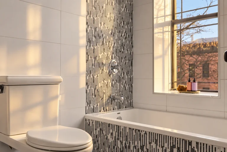 Bathtub and toilet beside mosaic tile and a window at 731 Putnam