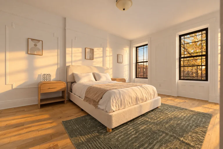 Bedroom with a white bed, wood nightstands, green rug and two tall windows in golden-hour light.