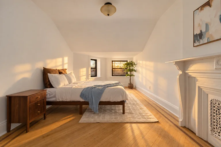 Bedroom with a sloped ceiling, wood bed, blue throw and a white fireplace surround.