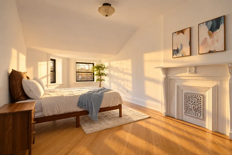 Warm afternoon bedroom view with a blue throw, paired abstract prints and a decorative white fireplace.