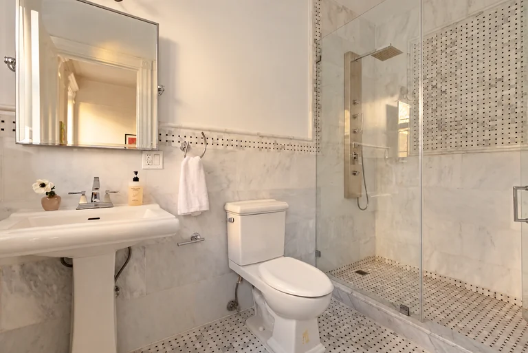 Marble bathroom with a pedestal sink, glass shower and soft warm reflected light.